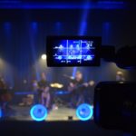 na pierwszym planie wizjer kamery w którym widać grających muzyków. tło dookoła rozmazane