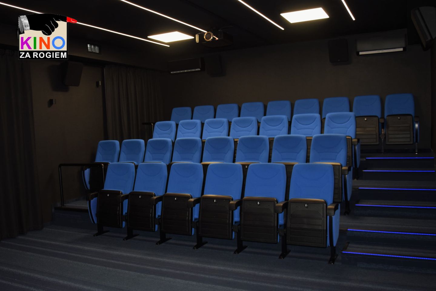 pusta widownia sali kinowej. niebieskie fotele i czarne ściany. w lewym górnym rogu logotyp kina za rogiem
