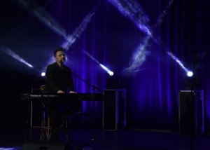 zdjęcie z koncertu, na scenie błękitne, krzyżujące się światła oraz dymy. na środku sceny jedyny muzyk, pianista i piosenkarz mateusz ziółko siedzący przy pianinie
