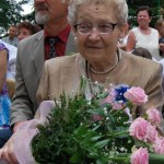 na zdjęciu założycielka zespołu rudniczoki - stefania redlich. starsza pani w krótkich siwych włosach i okularach trzyma bukiet kwiatów