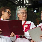 Na scenie znajdują się trzy starsze kobiety. Pierwsza o lewej i pierwsza po prawej trzymają teczki z zapisanymi słowami do śpiewu. Ubrane są w ludowe stroje.