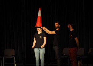Zdjęcie zostało zrobione w sali widowiskowej CKiB w Opalenicy. Na scenie widzimy trzech aktorów, jedną kobietę i dwóch mężczyzn. Kobieta ma założony na głowie słupek drogowy.