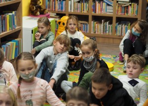 Zdjęcie zostało zrobione w bibliotece CKiB w Opalenicy. Na kolorowym dywanie siedzą dzieci.