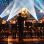 Zdjęcie zostało zrobione w kościele św. Mateusza w Opalenicy. Na pierwszym planie widzimy dyrygenta odwróconego plecami do aparatu, który został sfotografowany w ruchu. Przed nim za pulpitami siedzi orkiestra, która gra utwór.