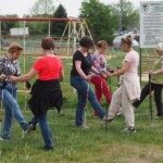 panie z kijkami nordic walking wykonują ćwiczenia rozgrzewkowe, stoją twarzami do siebie i podnoszą na zmianę nogi