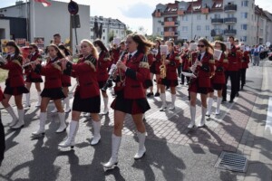 orkiestra gra oraz idzie ulicą, muzycy ubrani są w czerwone mundury