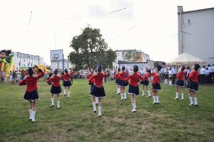 mażoretki ubrane w czerwone stroje występują, na zdjęciu podrzucają pałeczki mażoretkowe