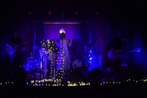 zespół grający na przyciemnionej scenie, punktowo świecą się tylko ozdobne lampki