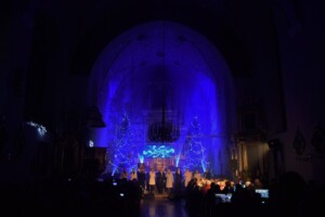ujęcie na występujący zespół wokalny, w tle widoczny podświetlony na niebiesko ołtarz