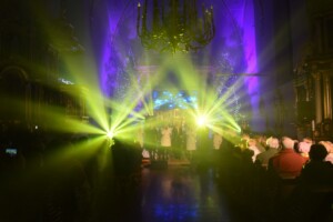 zespół wokalny podczas występu, z lewej i prawej strony promienie żółtego światła, które ubogacały koncert wizualnie