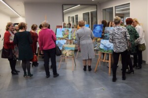 uczestnicy wystawy podziwiają obrazy, zdjęcie od przodu, widać plecy osób