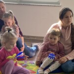 na zdjęciu mamy wraz z dziećmi siedzą na dywanie