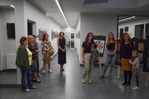 na zdjęciu uczestnicy wystawy stoją w holu podziwiając prace