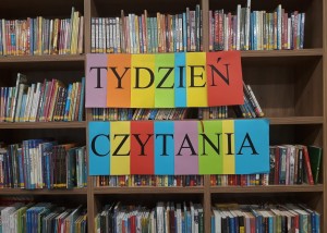 Zdjęcie zostało zrobione w bibliotece Centrum Kultury i Biblioteka w Opalenicy, na kolorowych kartkach napisane jest hasło Tydzień Czytania, napis został powieszony na regałach z książkami