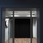 Zdjęcie zostało wykonane w drzwiach wejściowych do Studia Radia Centrum 11. Na zdjęciu widać drzwi z szybami wygłuszającymii i podłogę. Na górze zdjęcia znajduje się neo z napisem On Air. Napis jest biały na czerwonym tle.