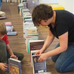 Zdjęcie zostało wykonane w bibliotece CKiB. Na zdjęciu kobieta w czarnych włosach po prawej stronie i chłopiec w jasnych włosach układają domino z książek.